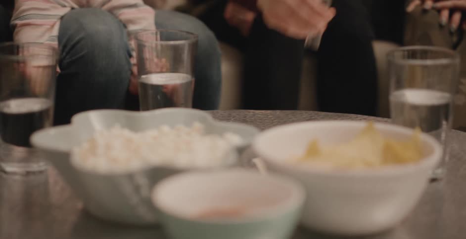 Parent bounces child on knee as another person flips sand glass on table near snacks