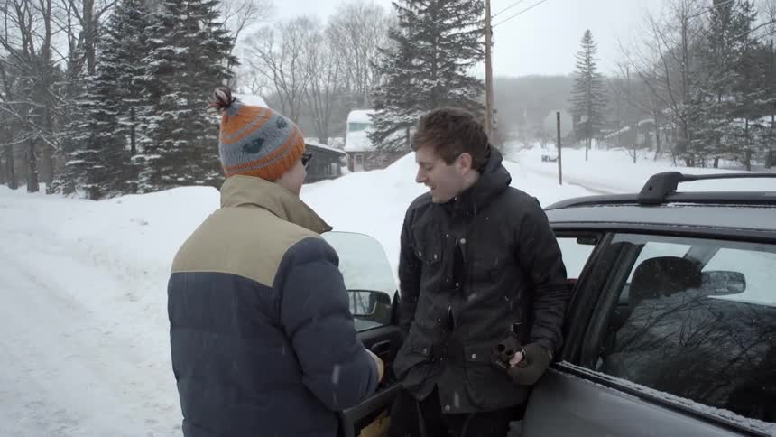 A man walks over to his car to greet another man