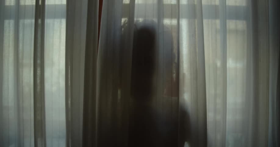 A person is standing in a window behind a curtain