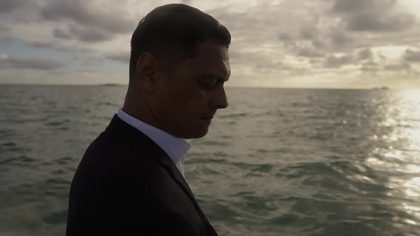 Man wearing business suit frowns while standing on shore on a cloudy day