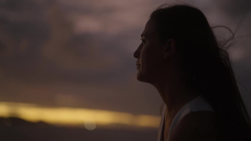 A woman outside enjoying a sunset on a cloudy evening