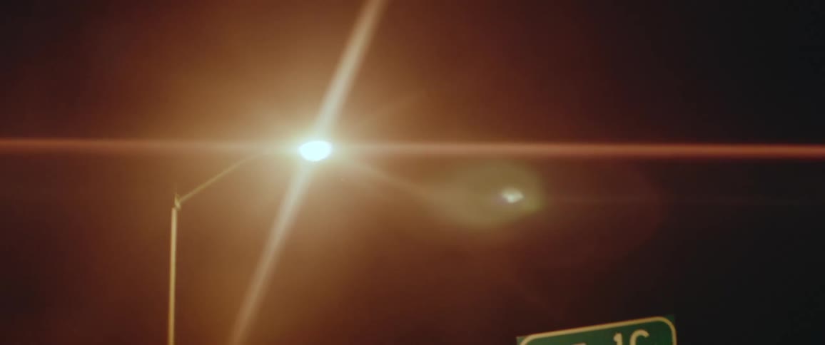 Moving on a freeway at night as light shines on the road signs above