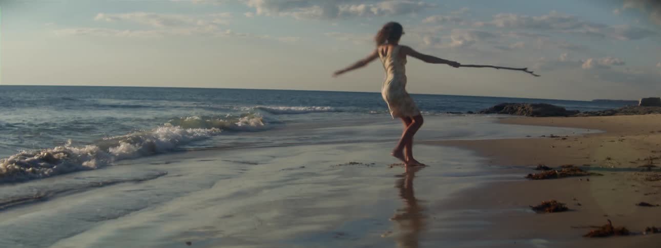 A woman spinning in circles with a stick on a sandy beach