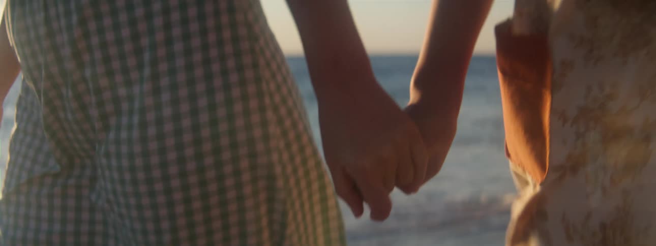A couple is holding hands and walking down the beach together