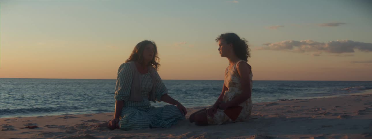 A woman is sitting on the beach with her teenage daughter as the waves roll into shore