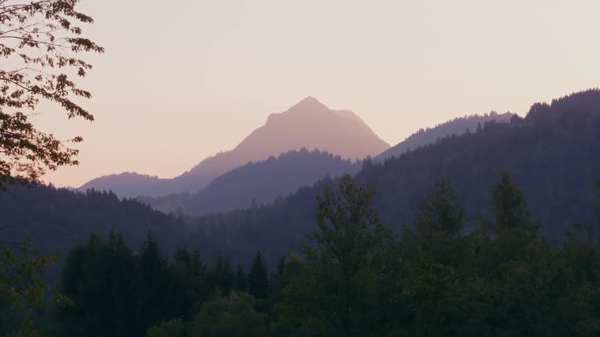 A distant fog shrouded mountain peak looms over a vast forest in the evening