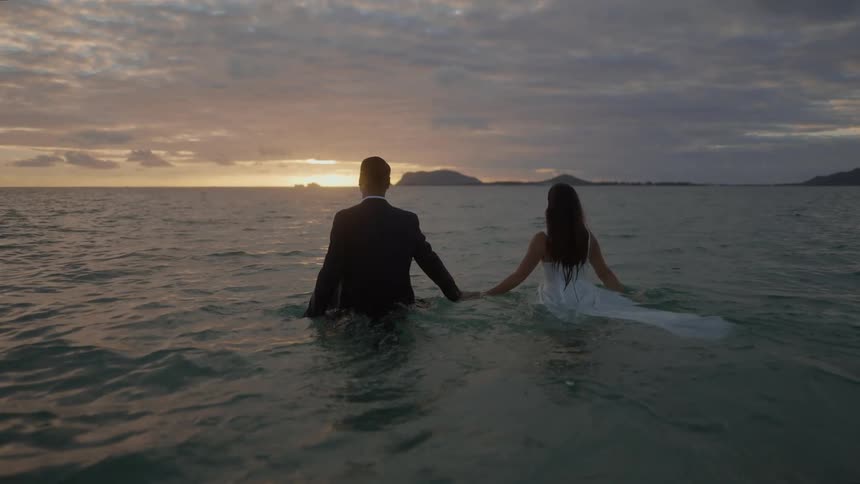 Bride and groom walk into the ocean together during their wedding