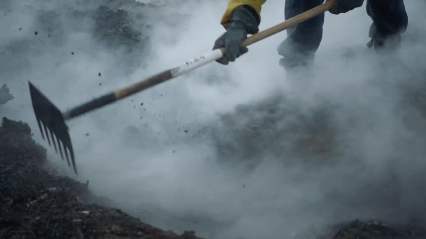 A person using a rake to rake dirt and gravel while steam and water roll through