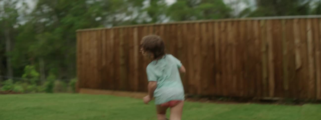Kid runs around on grass in backyard as adults watch from porch