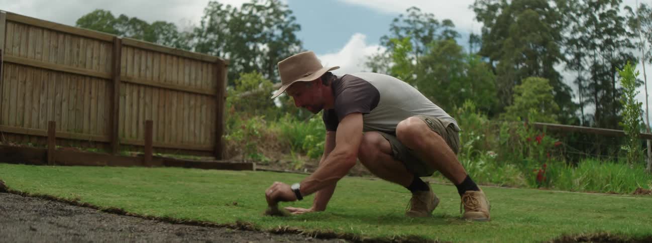 A man wearing a gardeners hat placing grass sod and arranging it