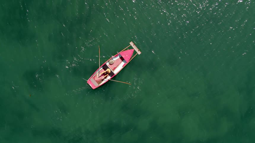 A woman rows a boat across a bluegreen body of water during the day