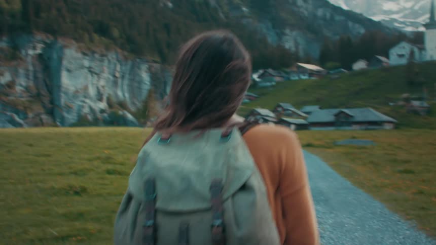 A backpacker walks down a trail below snow capped mountains