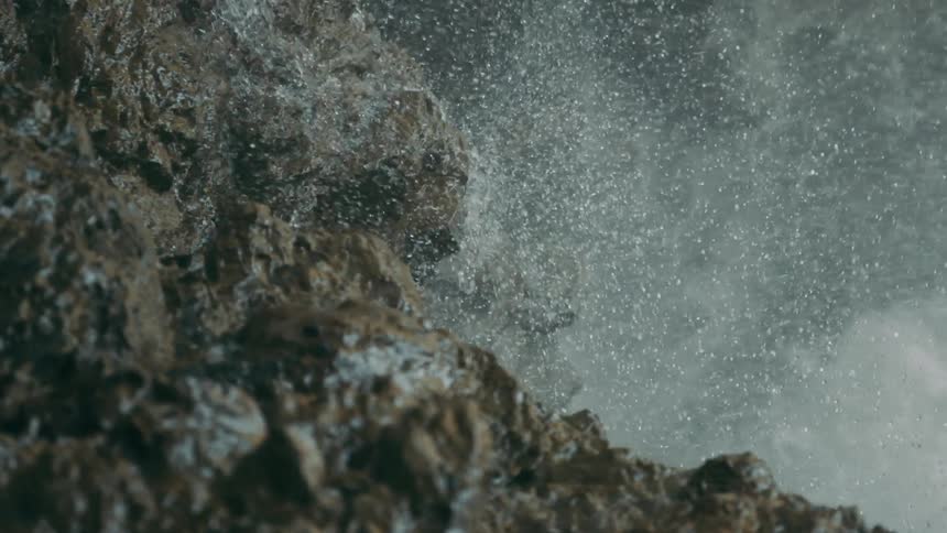 Snow floats through air and lands on stone on mountain side