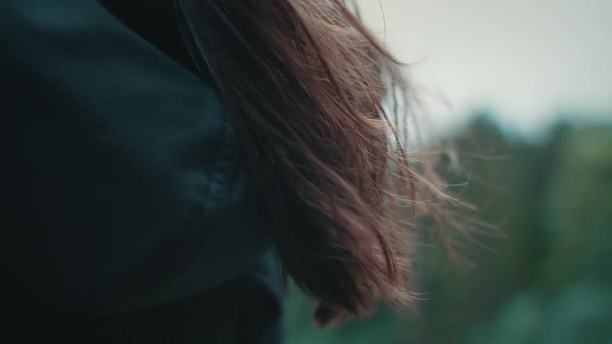 The wind blows on a girls long brown hair as it hangs outside of her hood