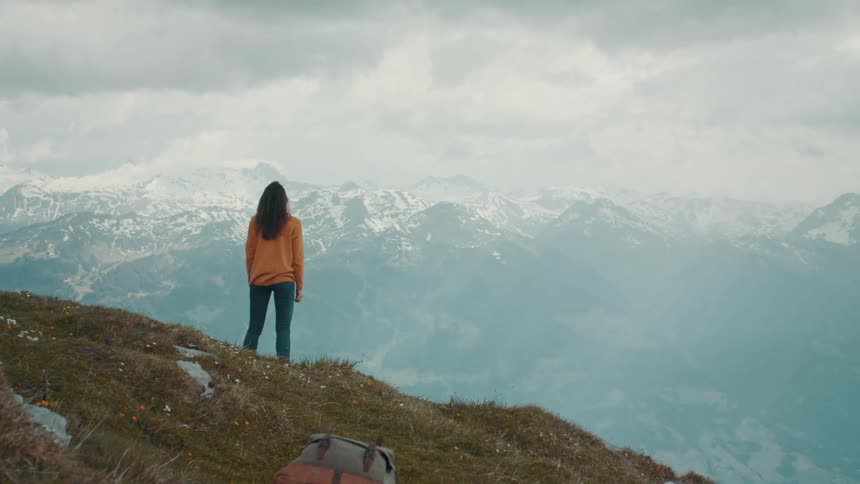 A woman stands atop a mountain and holds her arms outward