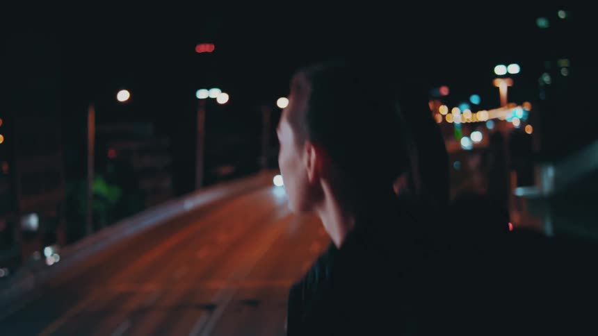 A woman walks along an overpass above a busy roadway at night