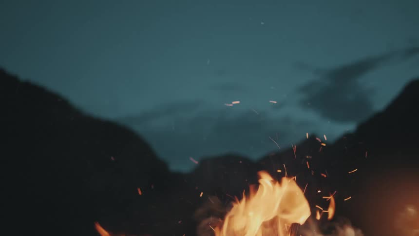 A fire burns and releases embers into the dark nighttime sky