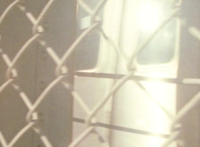 A passenger train passes by a chain link fence