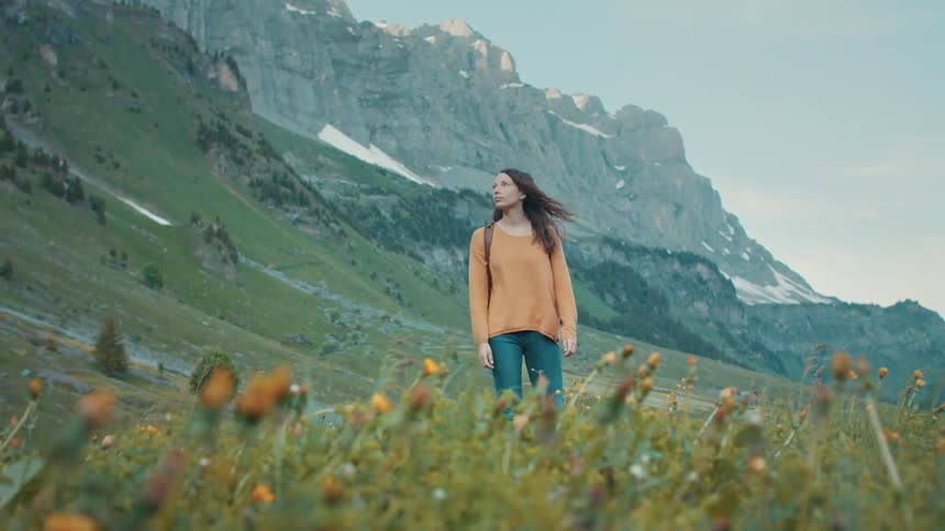Female backpacker stands on mountain slope near wildflowers