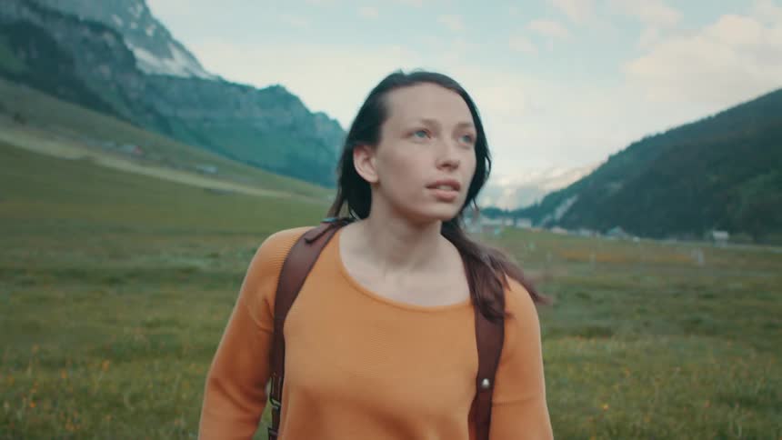 Female backpacker walks across field with town nestled between mountains in the background