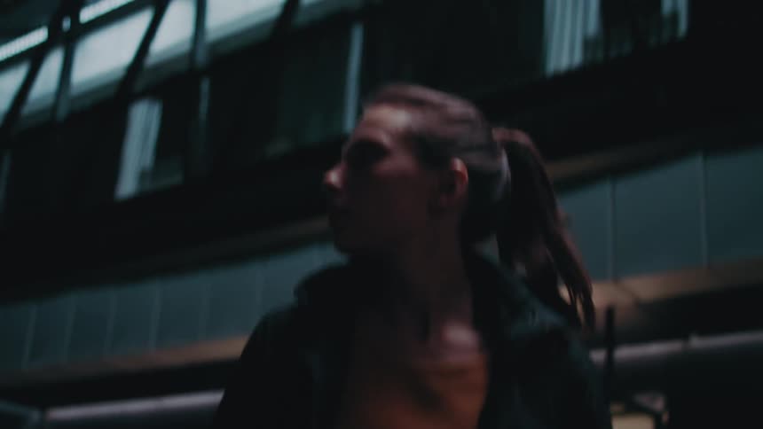 A young woman walks out of an office building at night and looks around