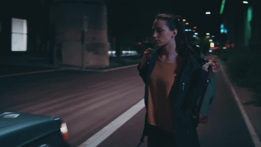 A woman walking down the side of the road in a black jacket getting into a car that pulls up