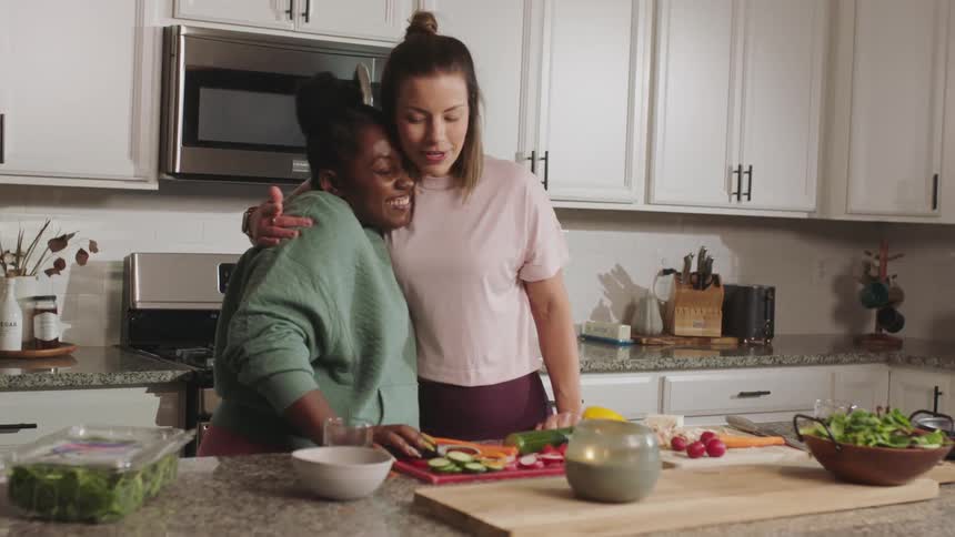 Two women standing in the kitchen preparing vegetables talking and laughing together
