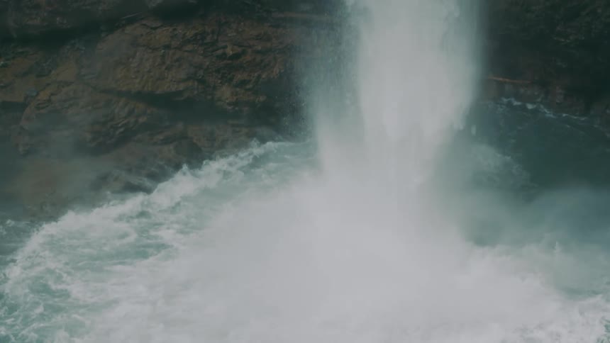 Waterfall flows down cliff to splash into pool spraying vapor into the air
