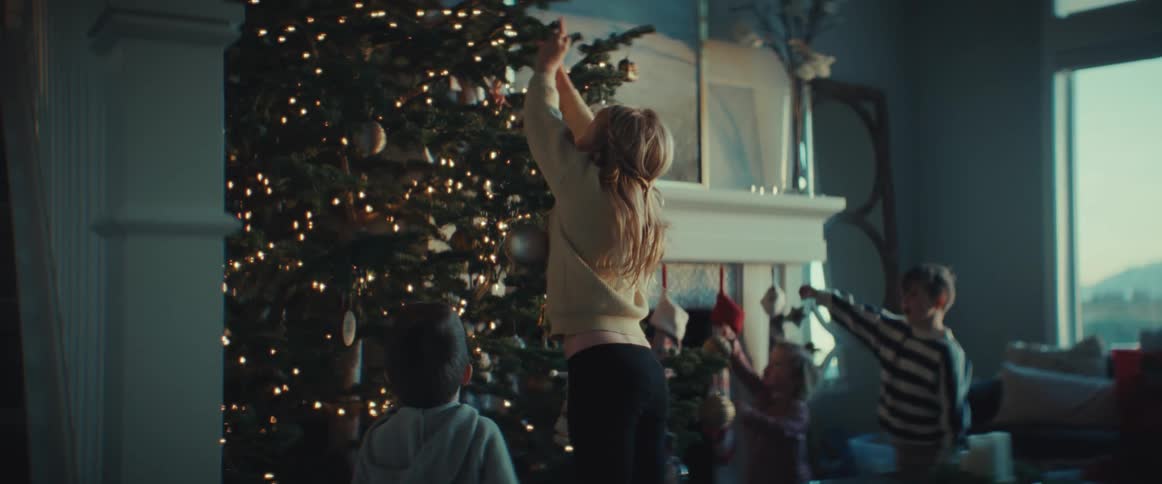 A pair of women decorate a christmas tree with a group of children