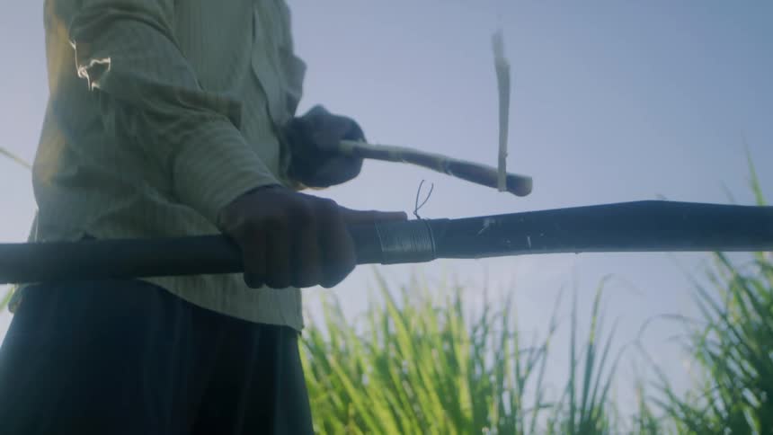 A man uses a sharp blade to peel bark off a stick