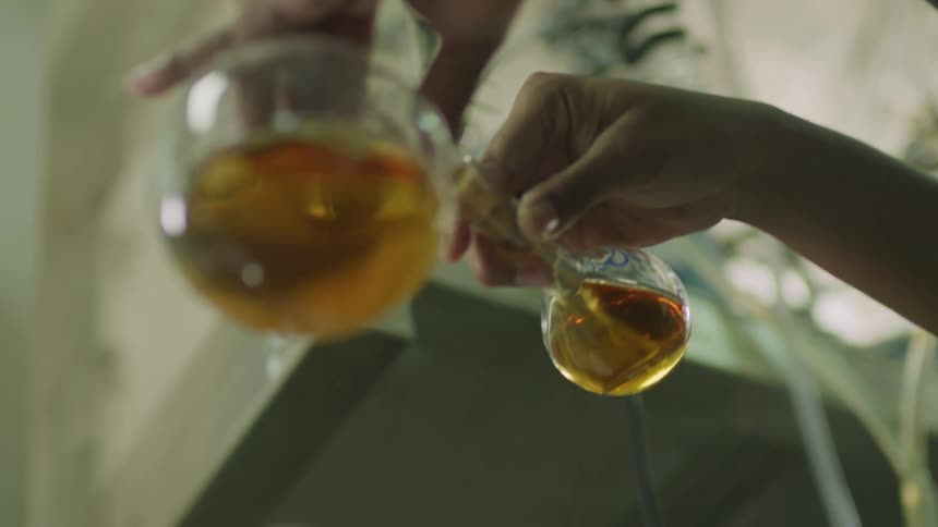 Person pours amber liquid from one glass container into another
