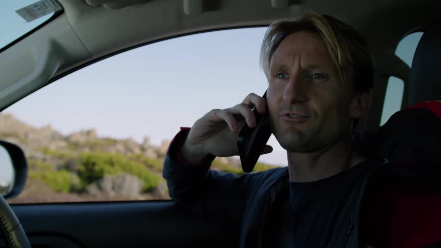 A man is sitting in his automobile talking on his cell phone