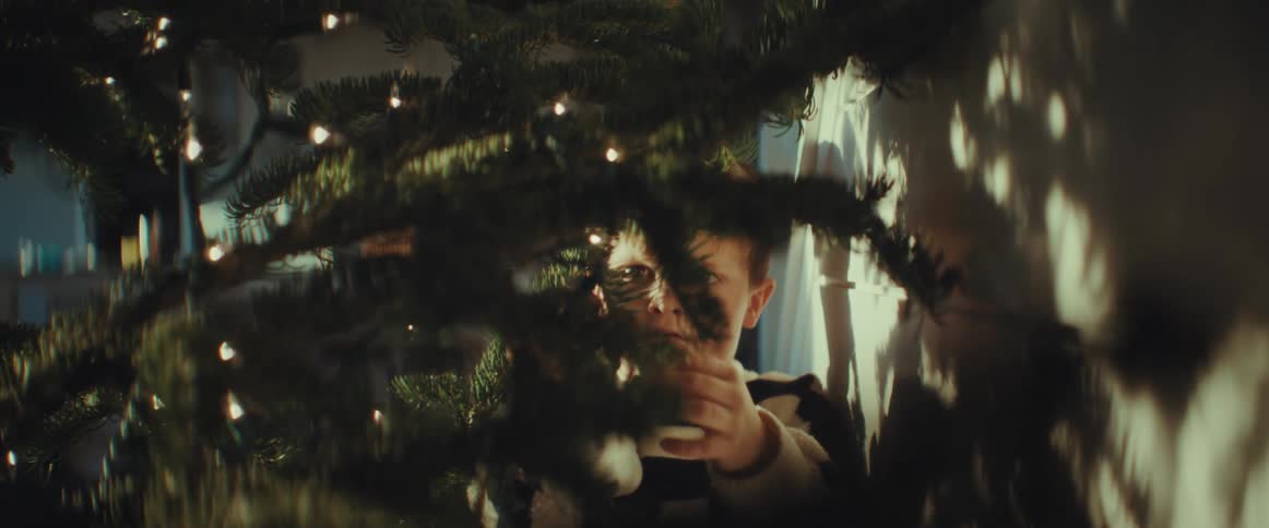 A little boy is hanging decorations on a christmas tree