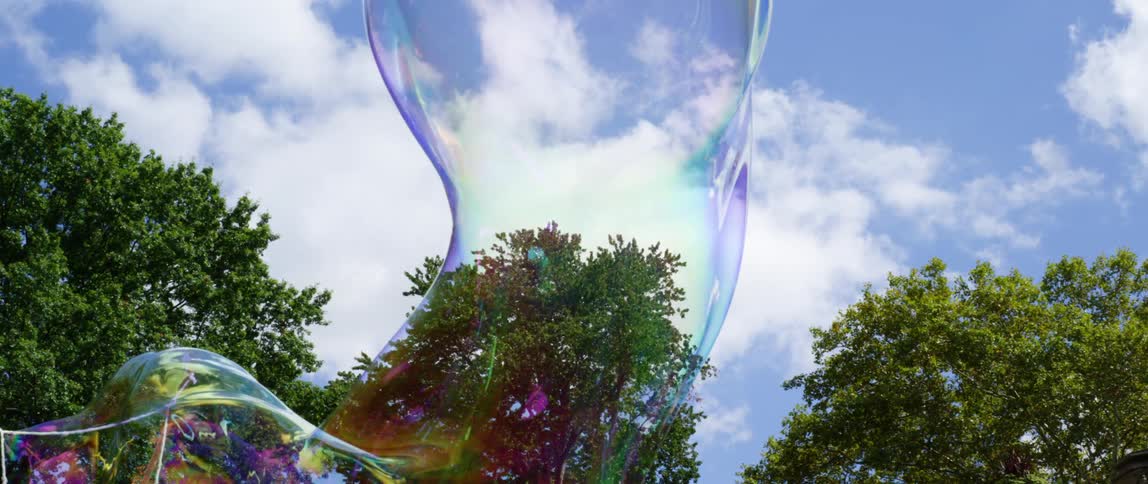 People watch as a large bubble is blown and floats outside and then pops