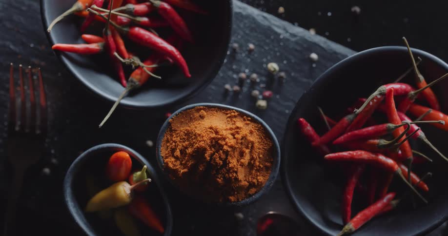 Hot chili peppers are in bowls on a table with a bowl of cayenne pepper