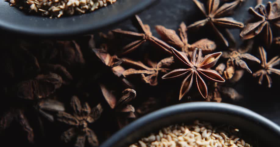 Star anise sits between two small black bowls filled with other spices