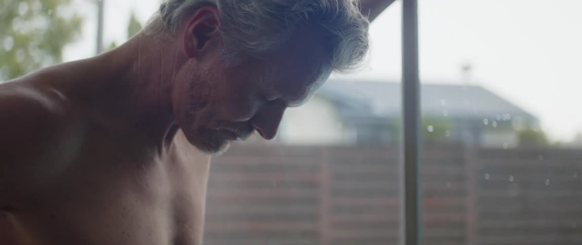 Man breathes deeply as he leans against glass window showing view of fenced backyard