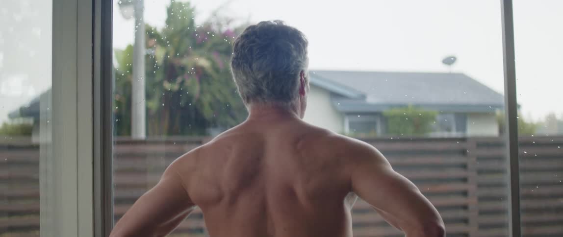 Older man walks toward floor length window and looks out