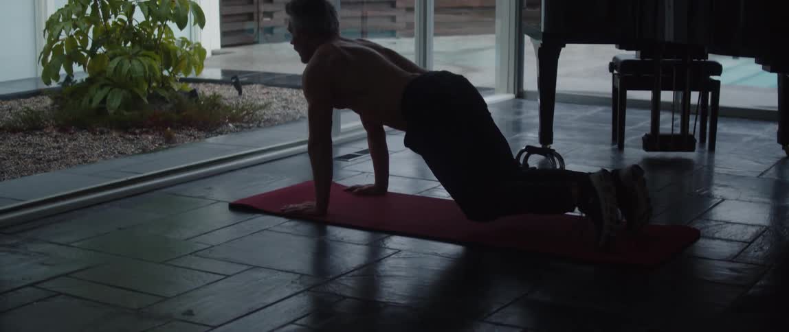 Topless muscular man works out on yoga mat next to grand piano in room