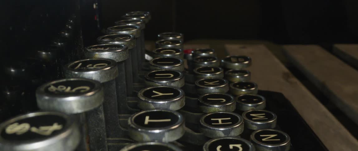 Manual typewriter with round keys sits on wooden slats in dim area