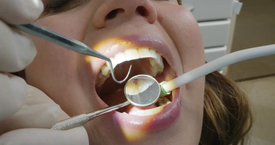 Dentist treats female patient using mouth mirror and explorer