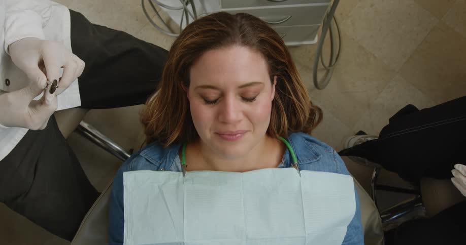 Seated dentist treats smiling female patient with the help of assistant