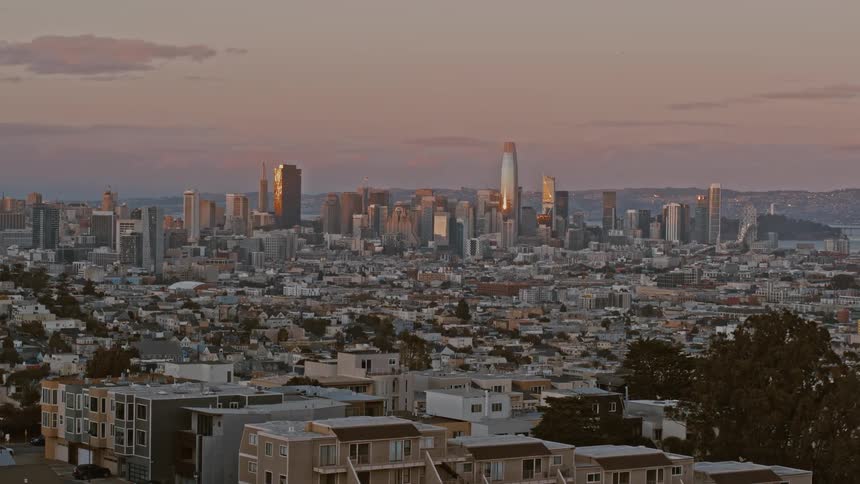 The sun sets on tall buildings in the downtown San Francisco skyline