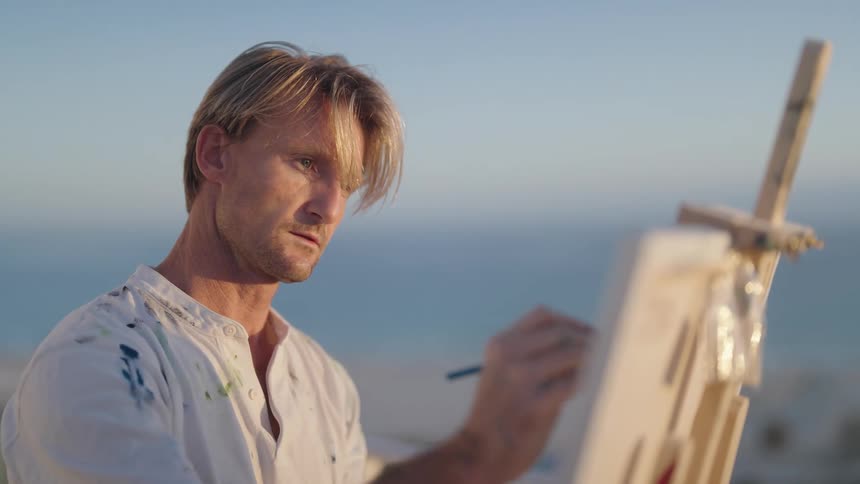 Blonde man paints canvas on easel pausing to study the scene