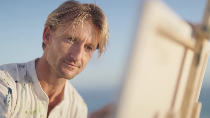 A man paints on a canvas outside