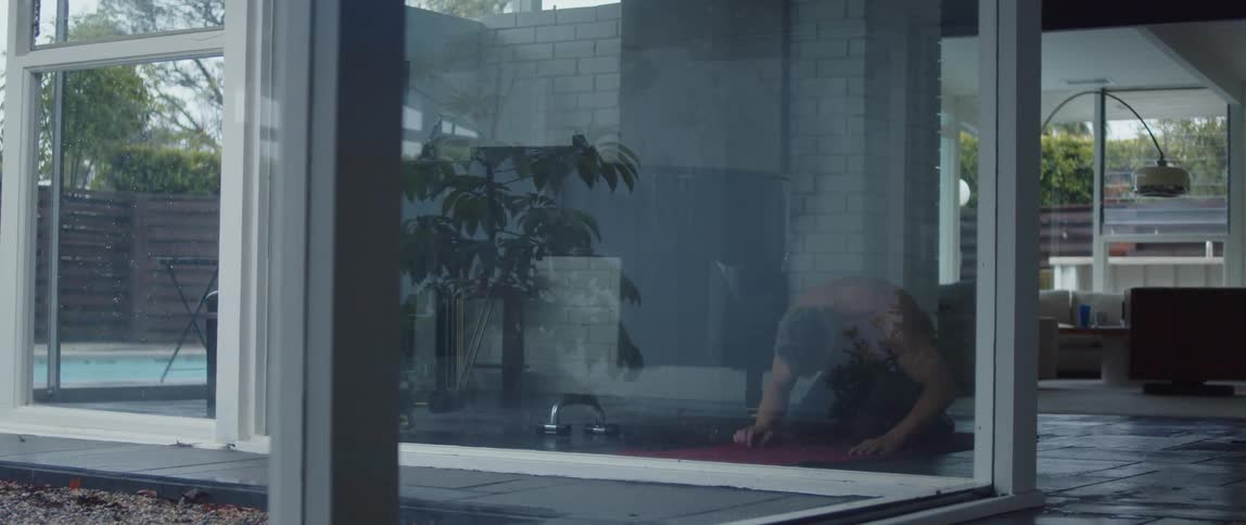 Topless muscular man stretches his body on yoga mat in the living room