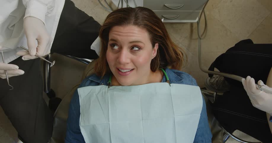 Seated dentist treats female patient using mouth mirror and explorer at dentist clinic