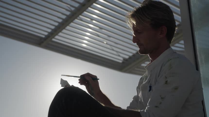 A man is sitting outdoors and is painting