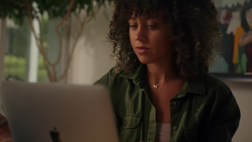 Woman sits in office taking notes while working on apple laptop
