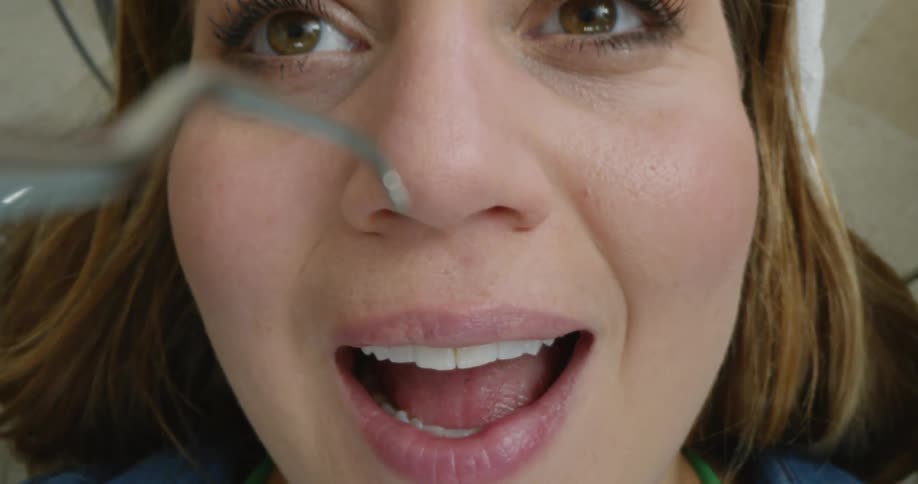 A woman in a dentists office opens her mouth as the tools get close
